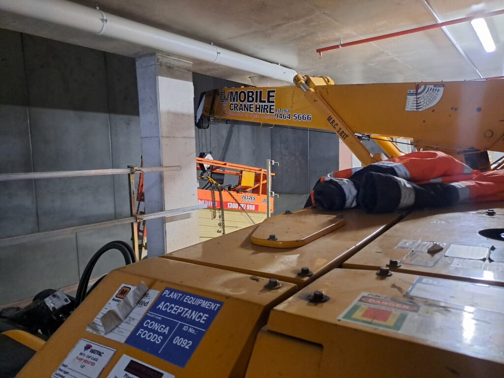 Tight access lifting. A scissorlift being lowered into position from a mezzanine floor in a carpark, avoiding the existing pipes